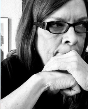 black white photo of neck length white haired female facing camera but looking to the left, hands folded on mouth